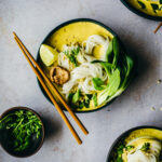 A bowl of creamy yellow curry soup with ricenoodles & green veggies
