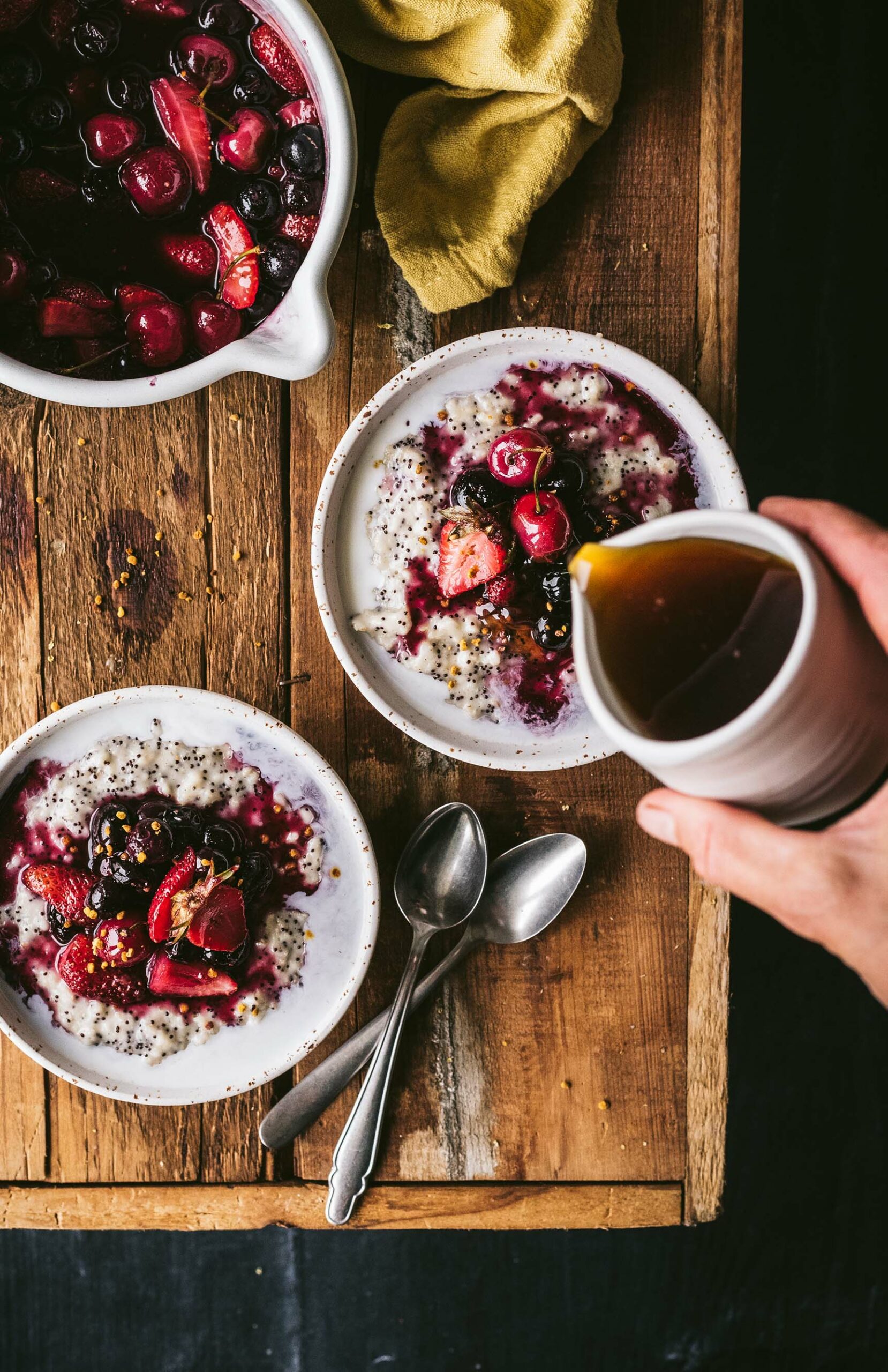 Pouring maple sirup over a creamy summer berry porridge.