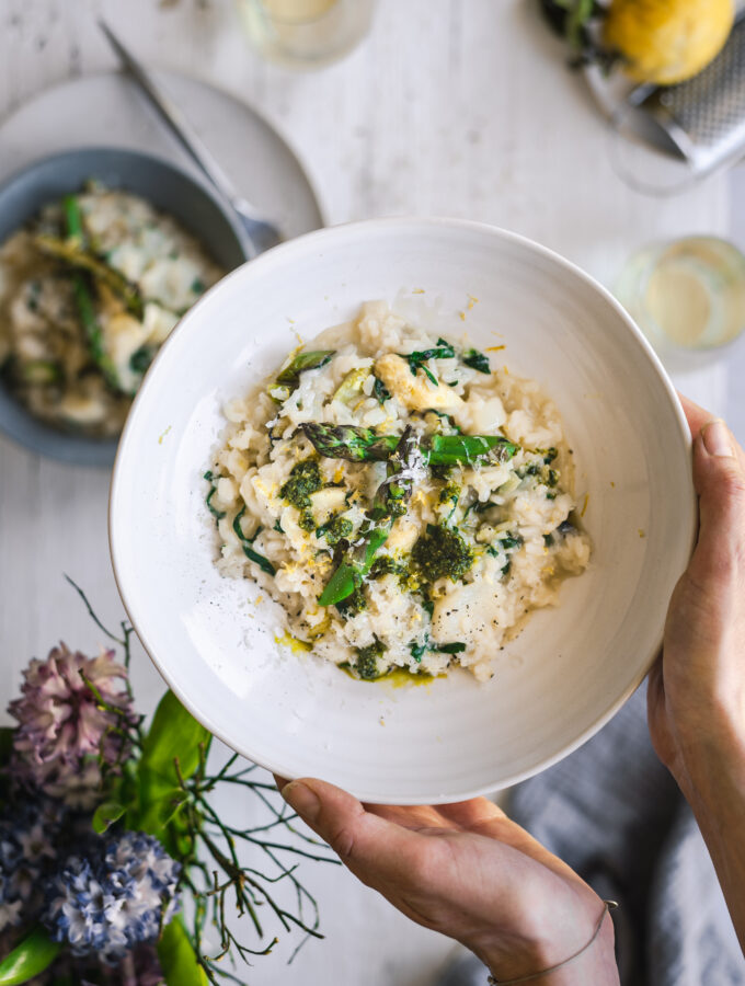 Holding a plate of creamy asparagus risotto with wild garlic pesto